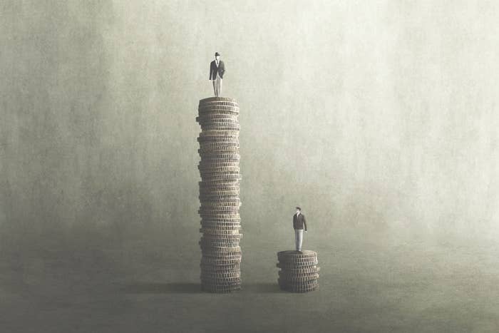 Drawing of one man standing on a tall pile of coins and another man standing on a short piles of coins to convey income inequality