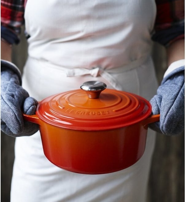 model holding orange colored Le Creuset cast iron dutch oven with lid on