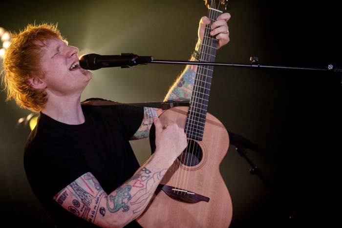 Sheeran strums a guitar and sings into a microphone during a performance