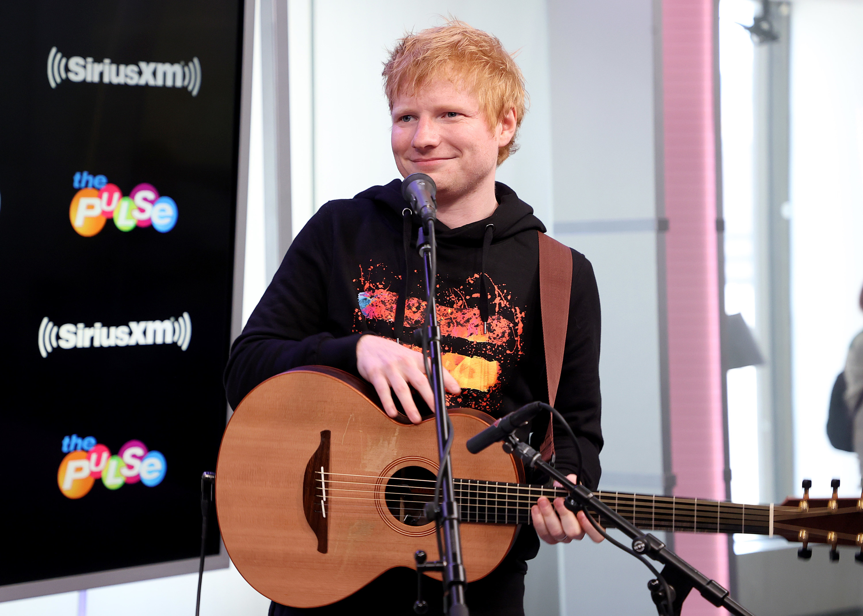 Ed Sheeran smiles with a guitar in a radio station studio