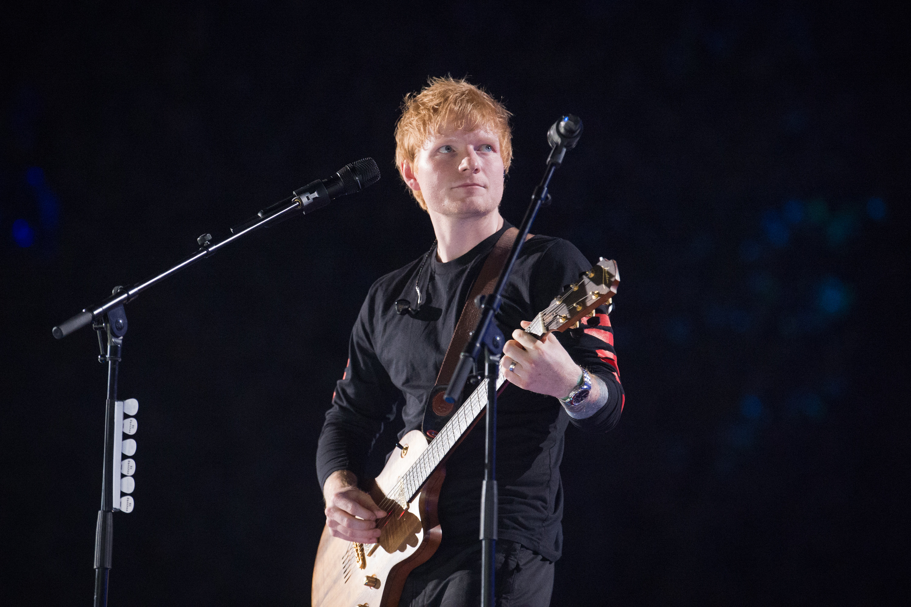 Sheeran looks off in the distance with a guitar in his hand onstage