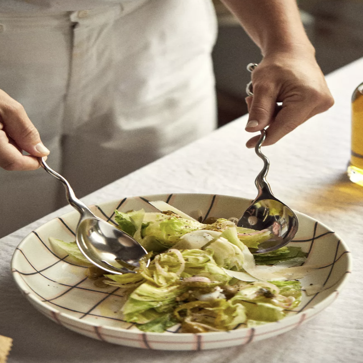 The serving utensils being used to mix a salad