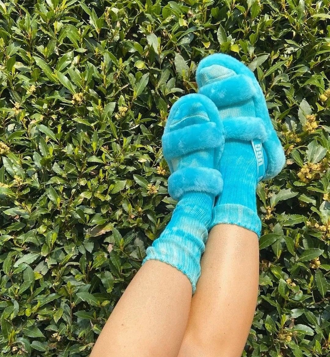 A person wearing the slippers with their feet up against a green wall