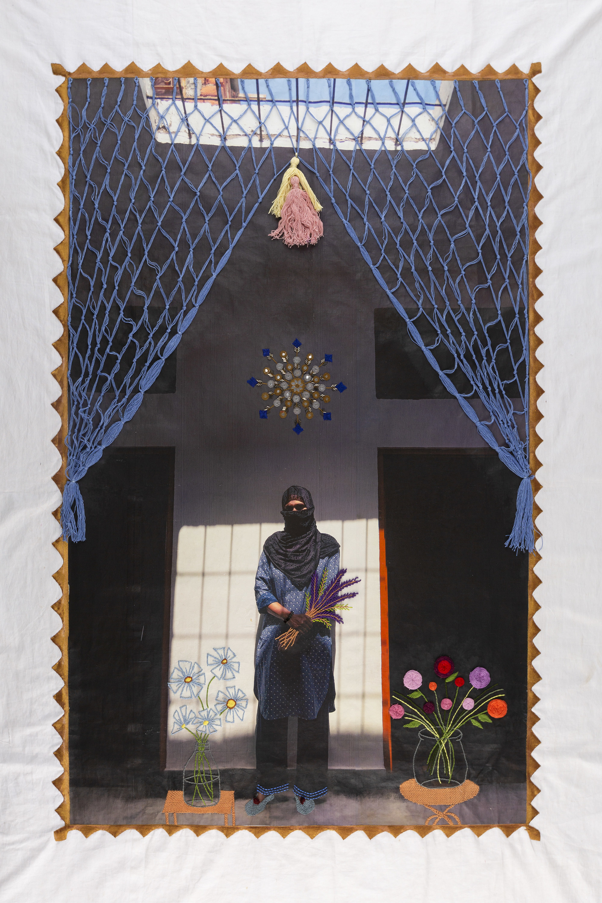 A woman stands in a room with two doorways, embroidered is a curtain, mandala, and flowers on tables