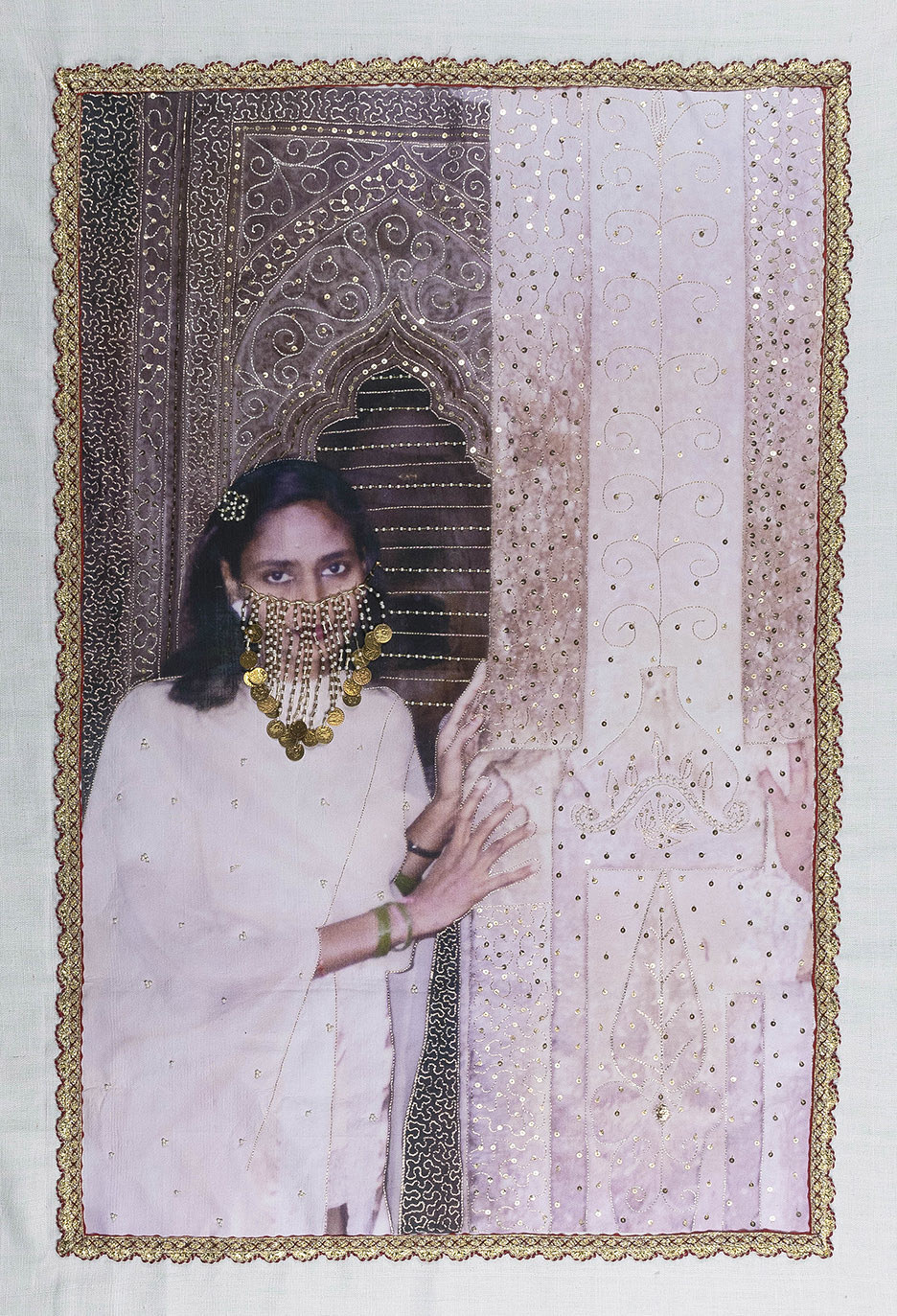 A woman stands next to an embroidered column, with an embroidered veil on her face