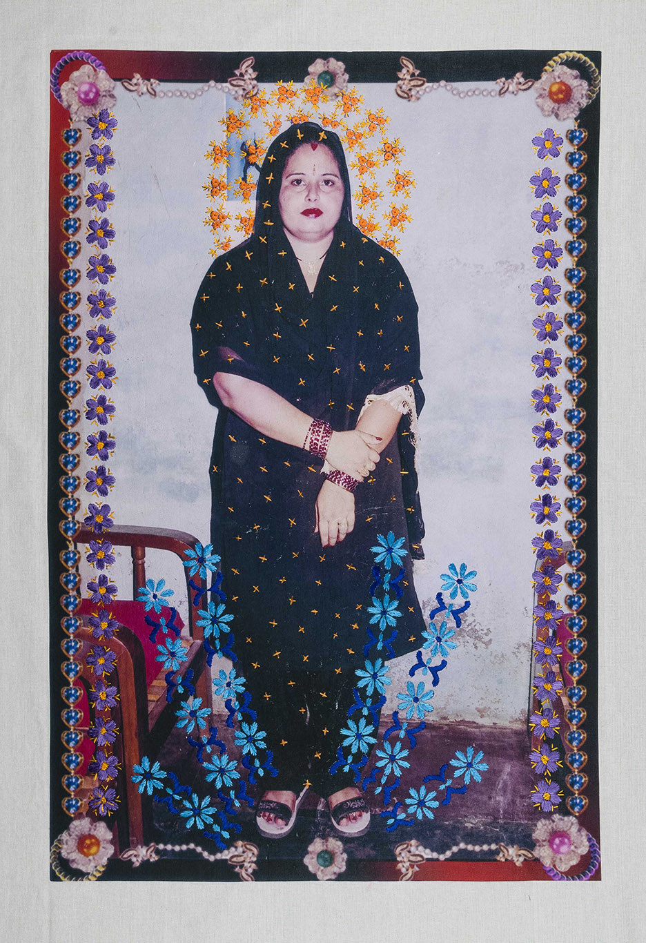A woman looks directly into the camera, her head covering and the border of the photo are embroidered