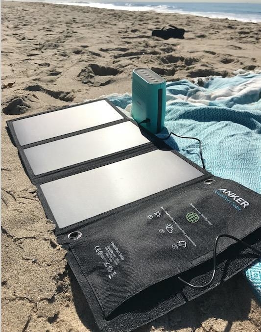 The solar-powered charger spread out on a beach, charging a portable speaker