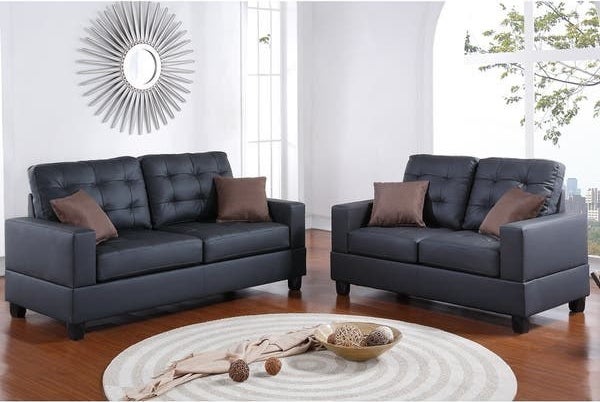 Product image of two black faux leather couches with brown pillows in front of a circle coffee table