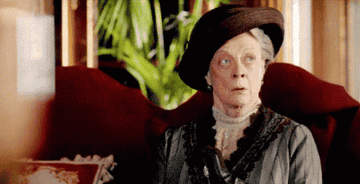 Maggie Smith sitting, wearing a hat, and looking shocked