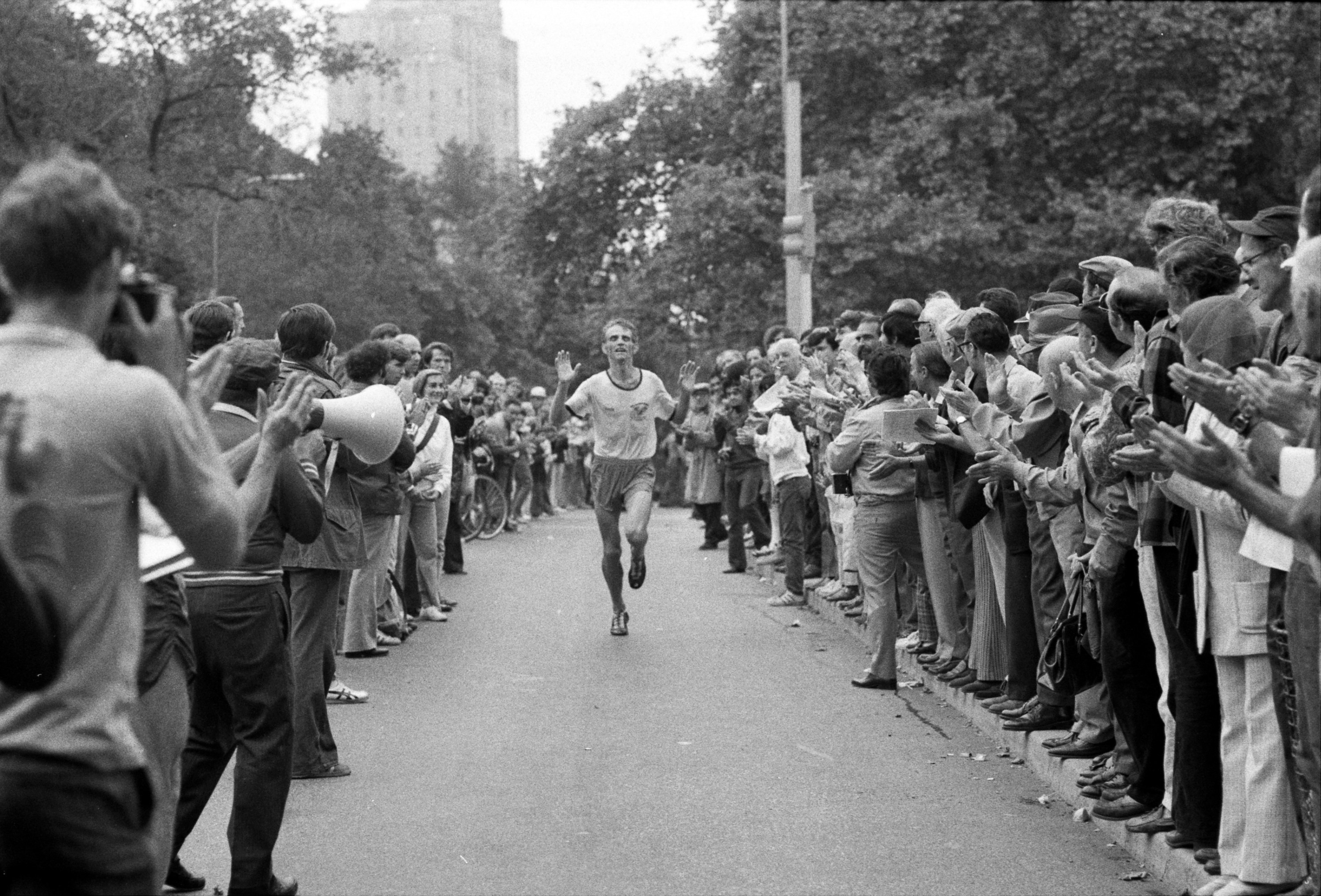 Black-and-white photo showing a man running toward the camera with crowds on either side