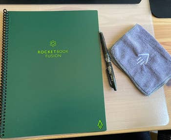 a reviewer photo of the closed notebook with the included pen and microfiber cloth