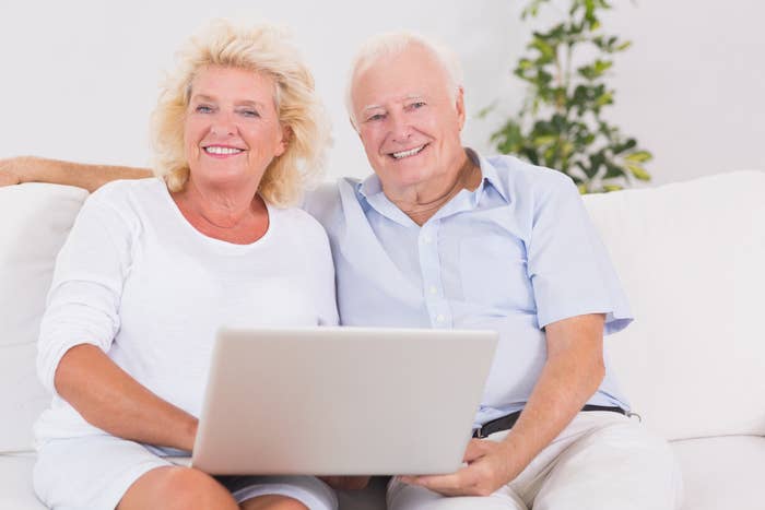 Smiling older people sitting on a couch with a laptop
