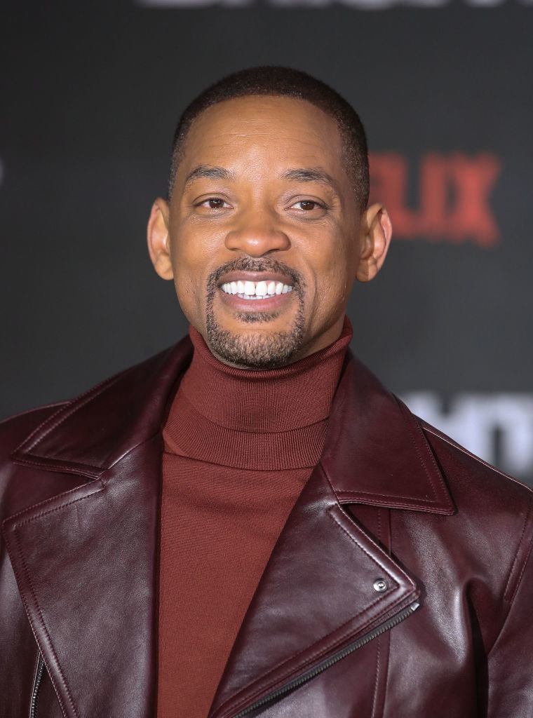 An older Will smiles at an event in a turtleneck and a leather jacket