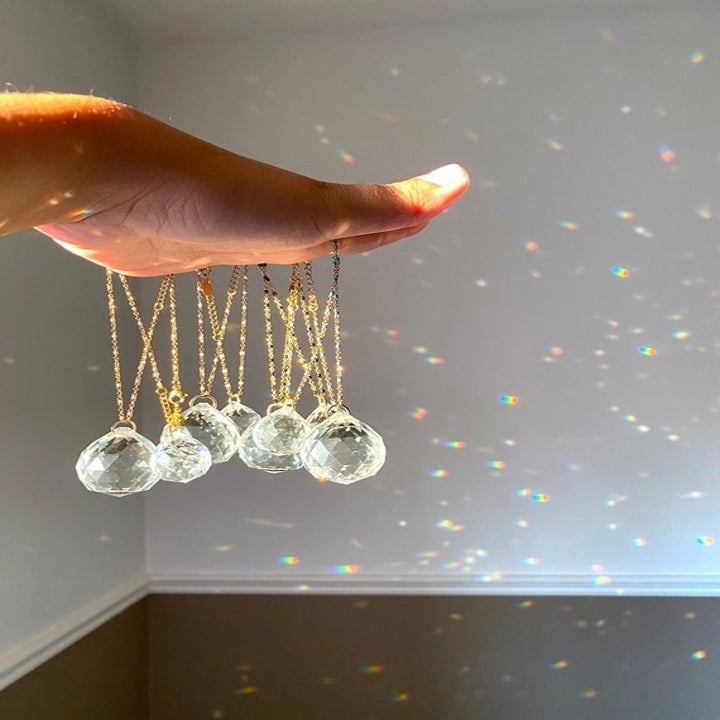 Hand holding multiple crystal sun-catchers to the light with them reflecting on a white wall