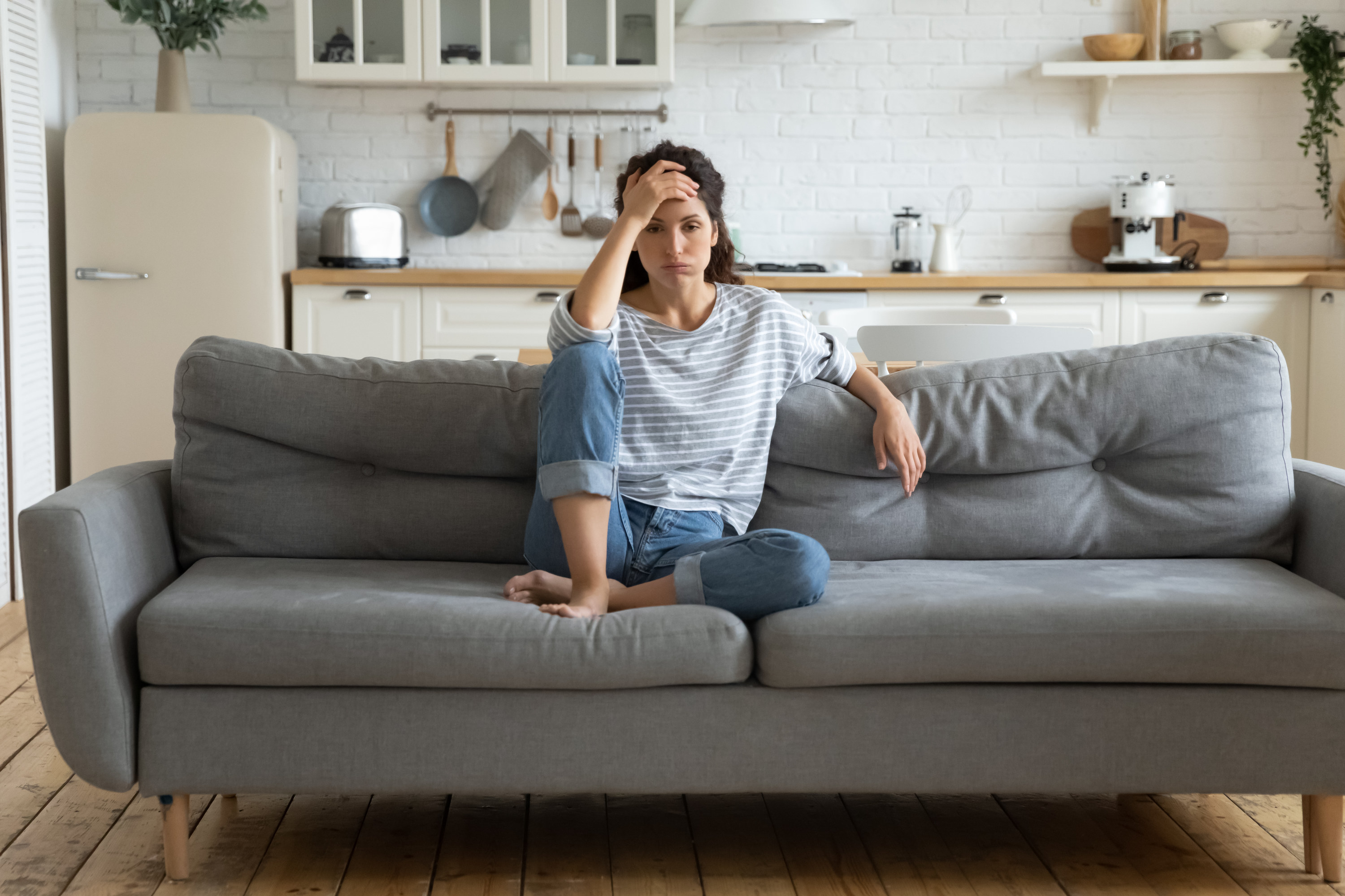 A woman looking stressed while sitting on her couch with her hand to her head