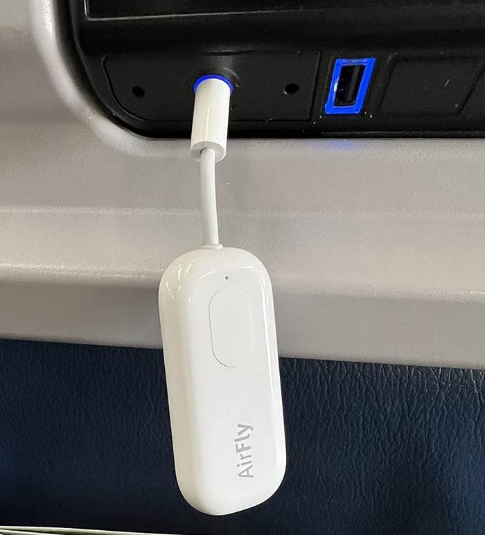 Reviewer photo of the AirFly Pro plugged into the headphone jack on the back of a plane seat