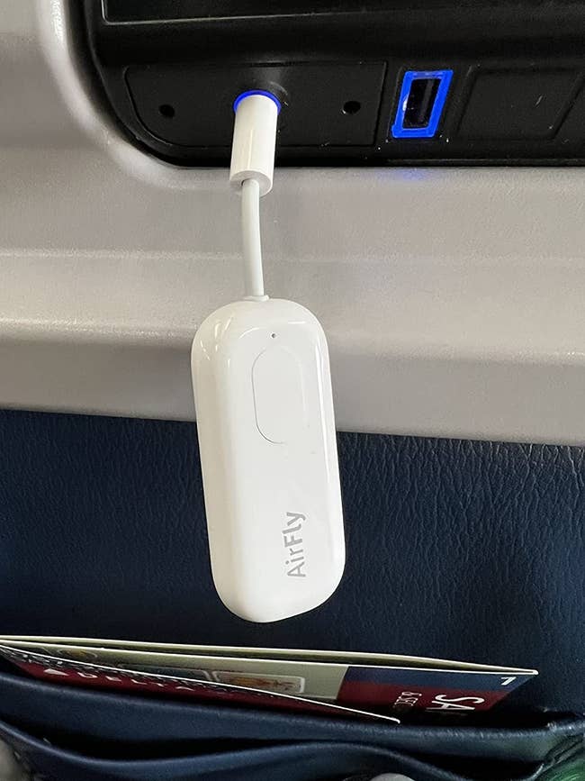 Reviewer's AirFly Pro plugged into the headphone jack on the back of a plane seat