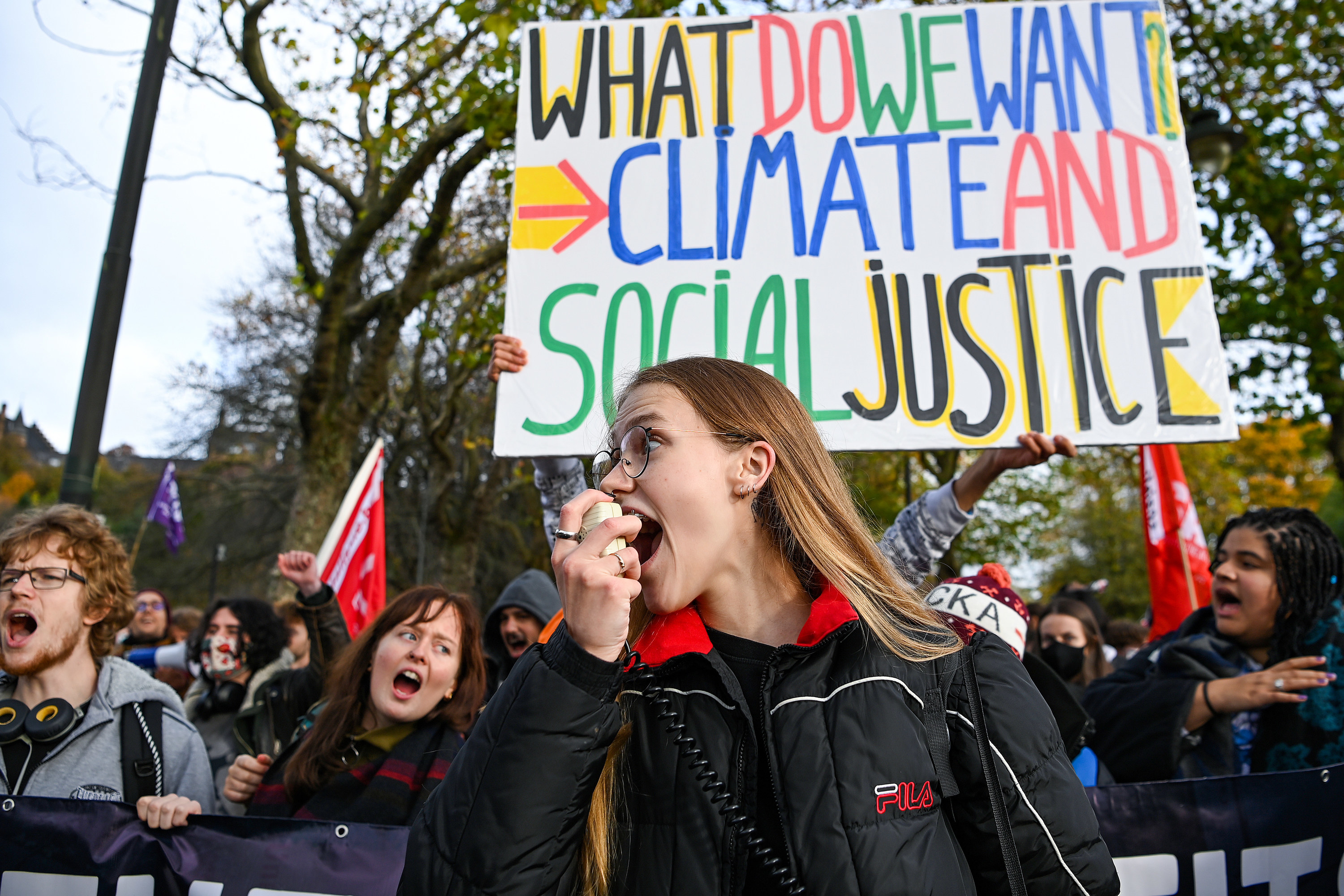 A young protester shouts into a megaphone in front of a sign that reads &quot;What do we want? Climate and social justice&quot;
