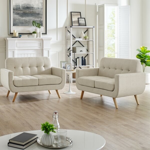 Two beige rounded couches on wood floor next to circle coffee table