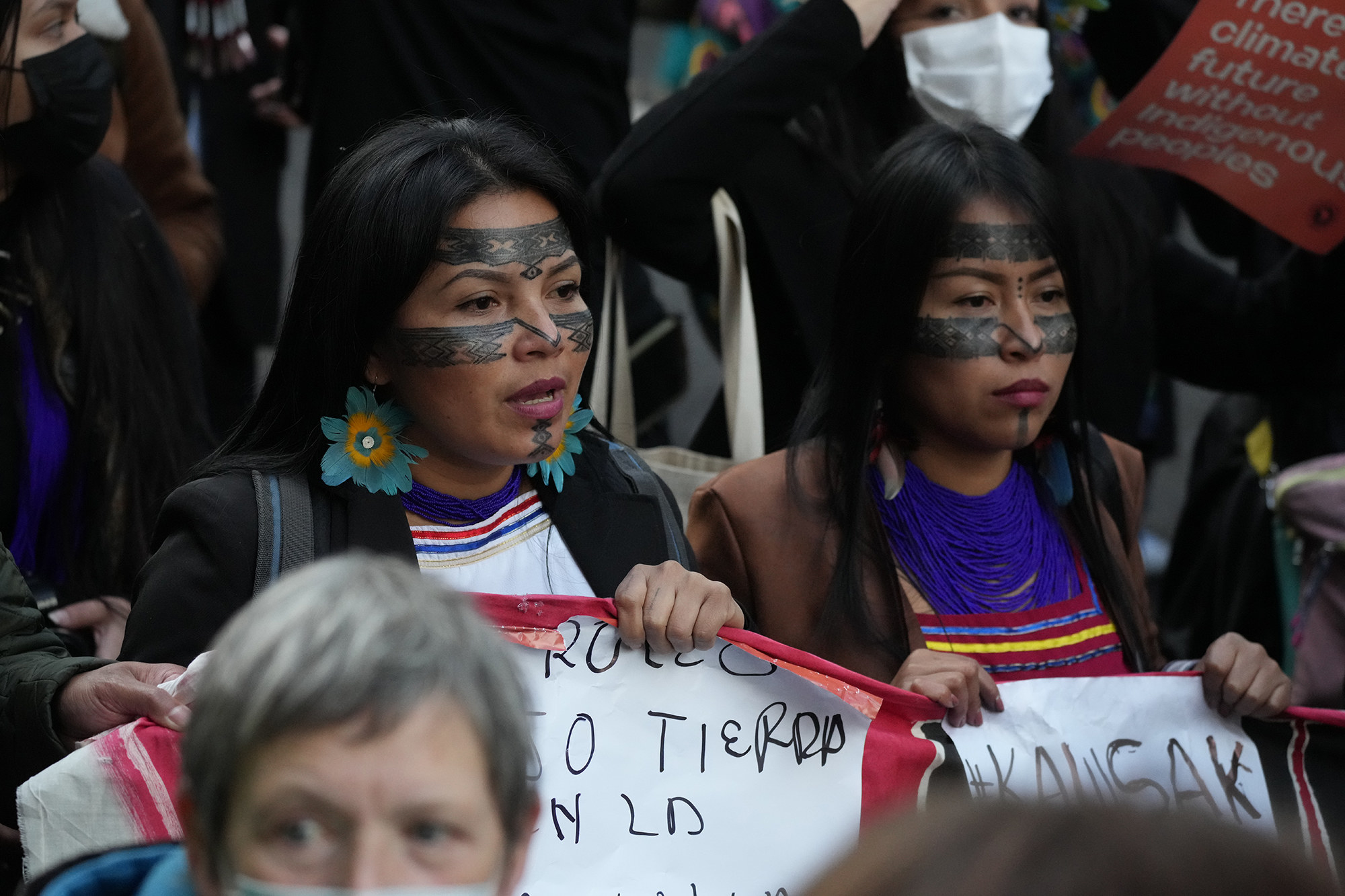 Two Indigenous women hold signs and wear face paint