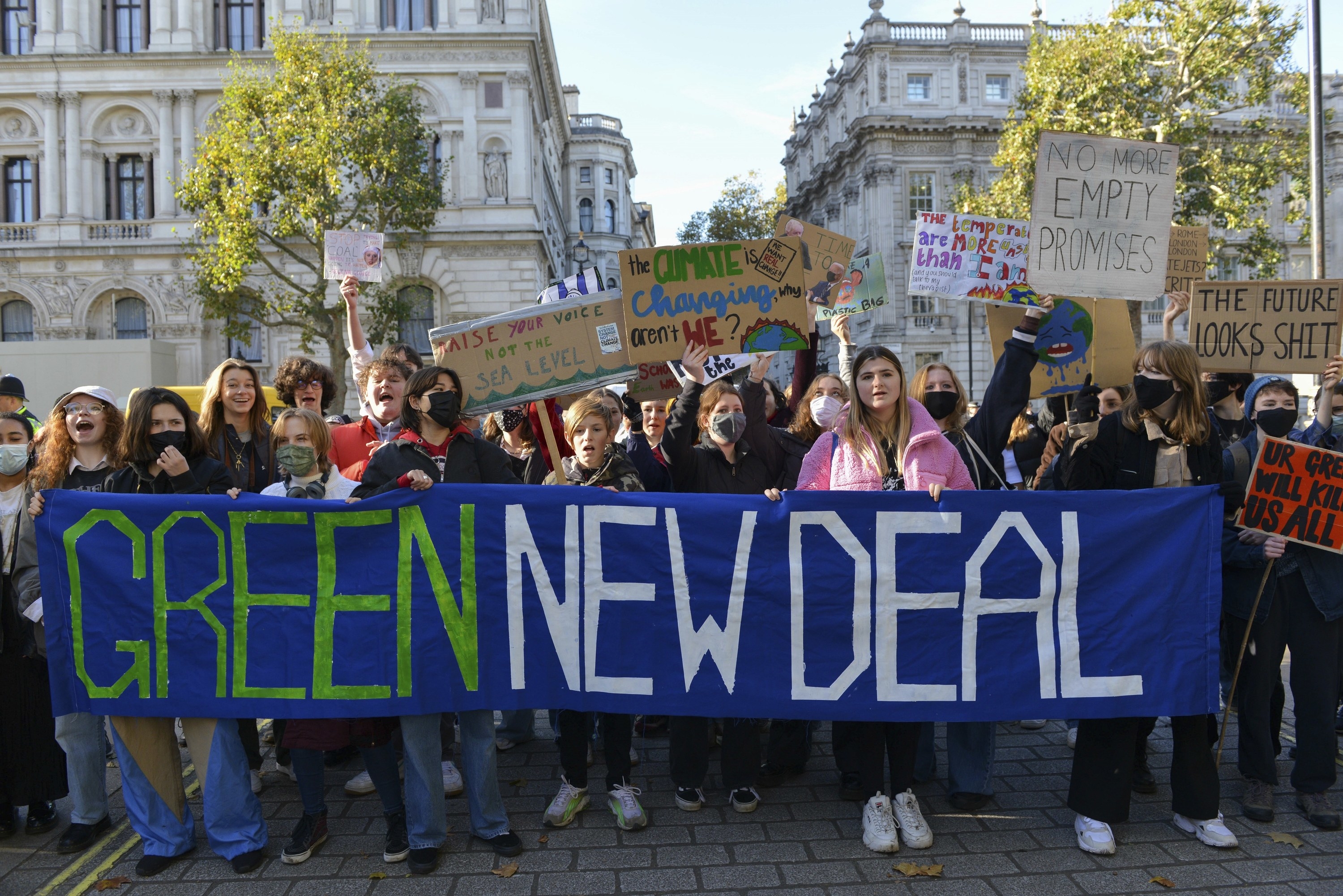 Protesters hold up cardboard signs and stand behind a banner that reads &quot;green new deal&quot;