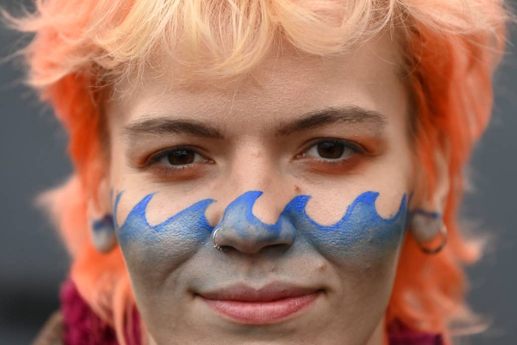 A young person wears face paint of waves that cross their cheeks and nose