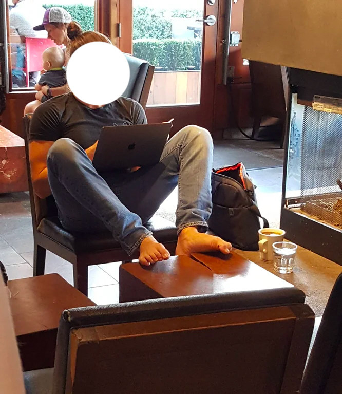 Someone at a coffee shop sits with their bare feet on the table