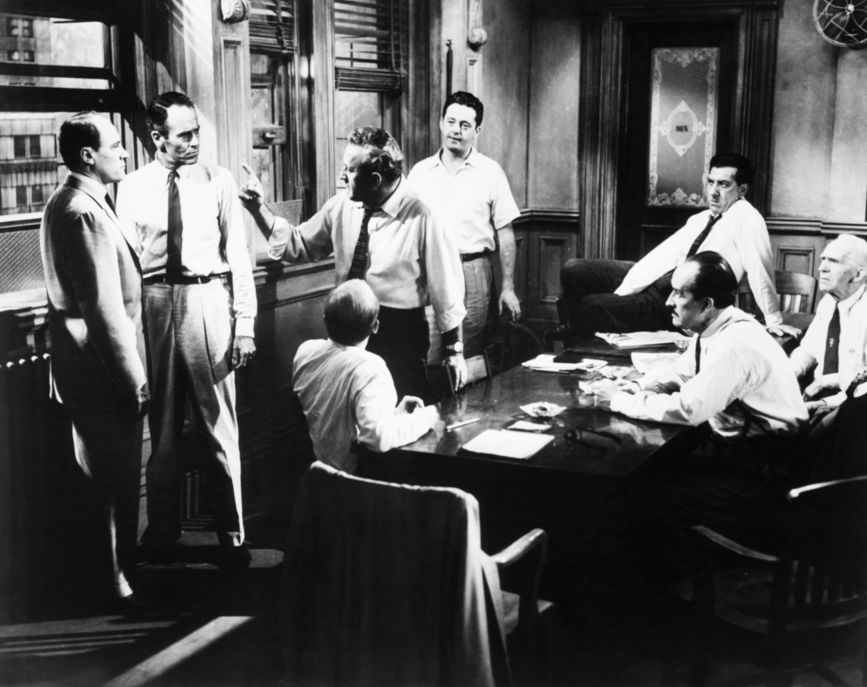A group of men argue in a small conference room