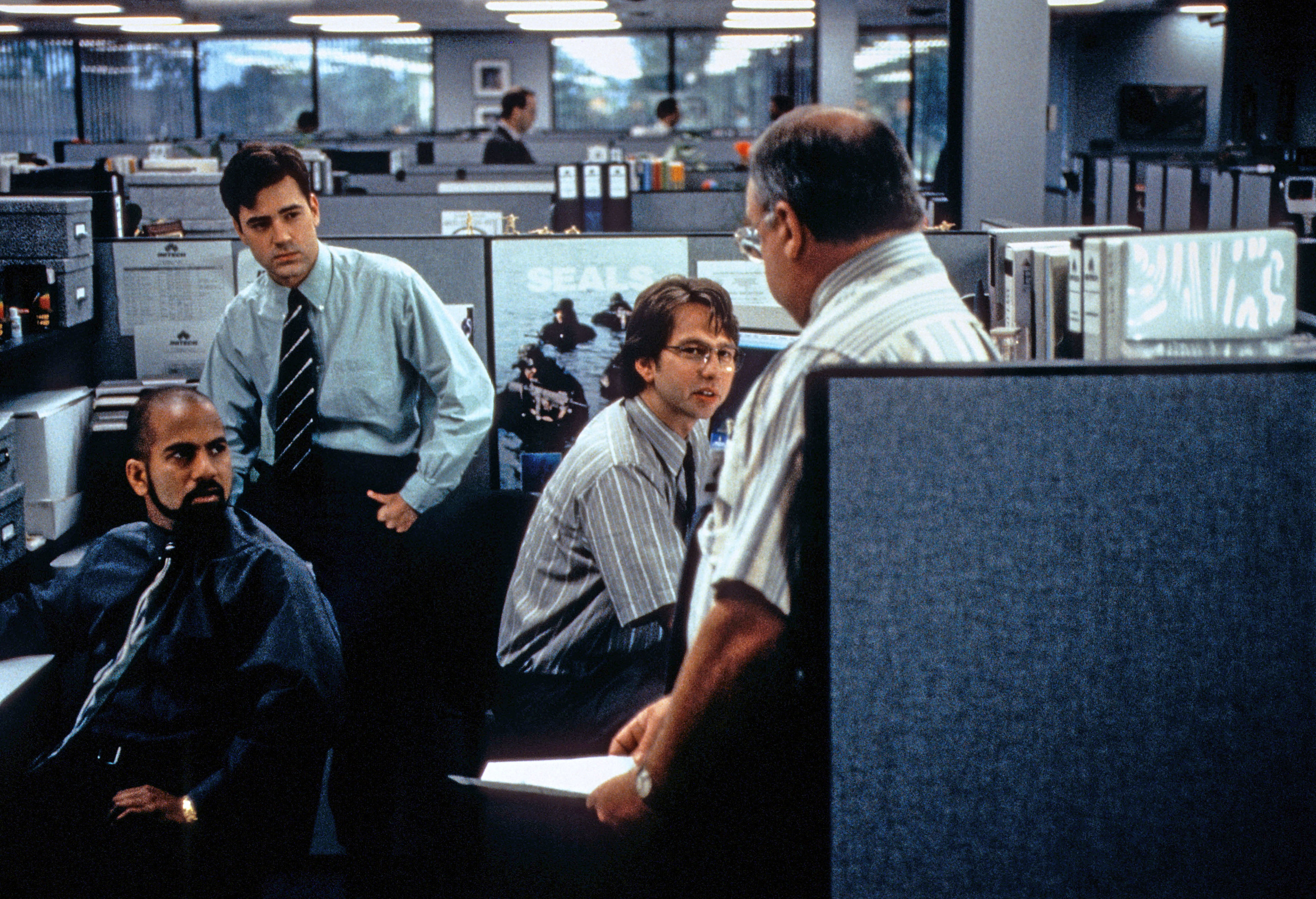A group of workers standing by an office cubicle