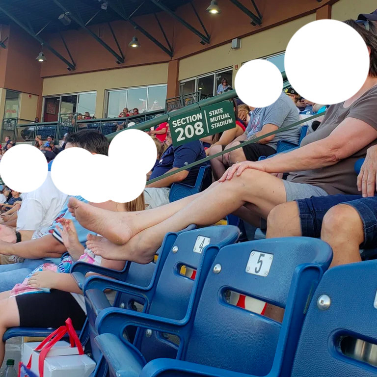 A woman puts her bare feet over the seat lower than her at a baseball game