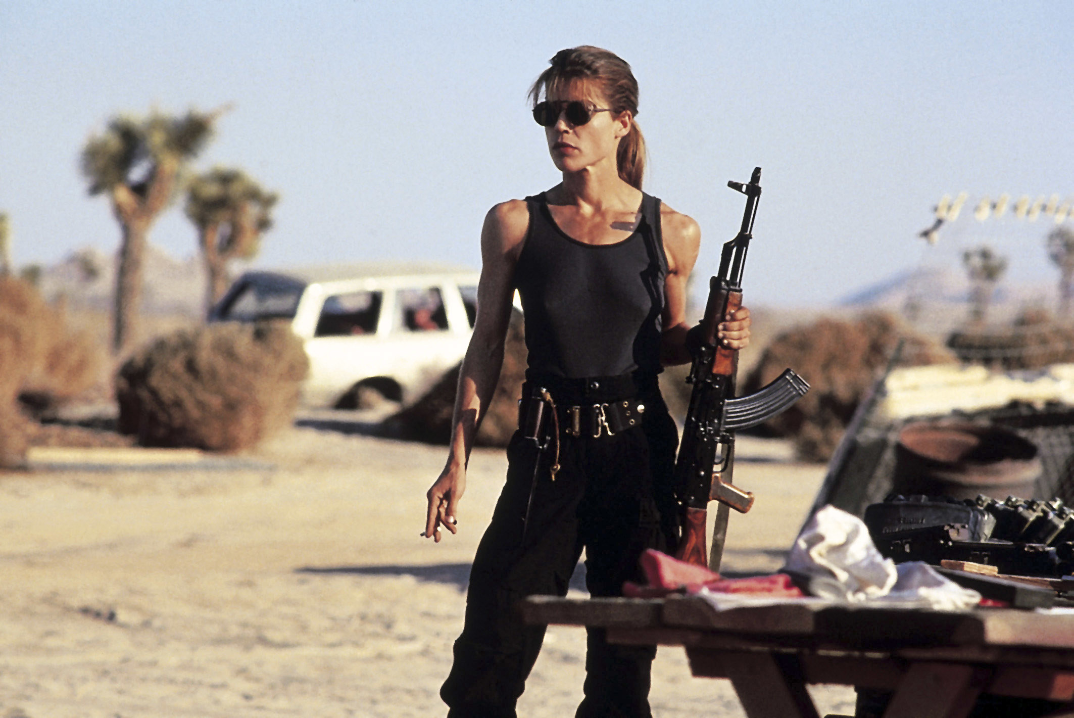 Sarah Connor standing in the dessert holding a rifle and looking bad ass