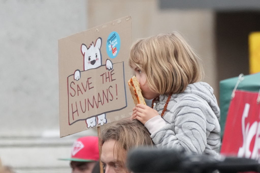 A young girl at the protest sitting on the shoulders of an adult with a sign nearby that says &#x27;Save the Humans&#x27;