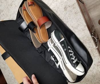 Reviewer showing the bag's shoe compartment filled with a pair of sneakers and two pairs of sandals