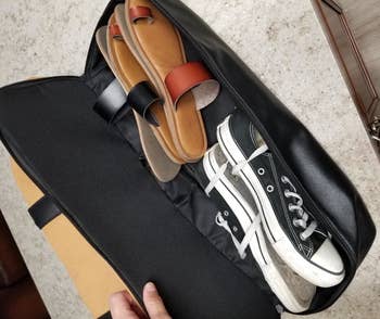 Reviewer showing the bag's shoe compartment filled with a pair of sneakers and two pairs of sandals