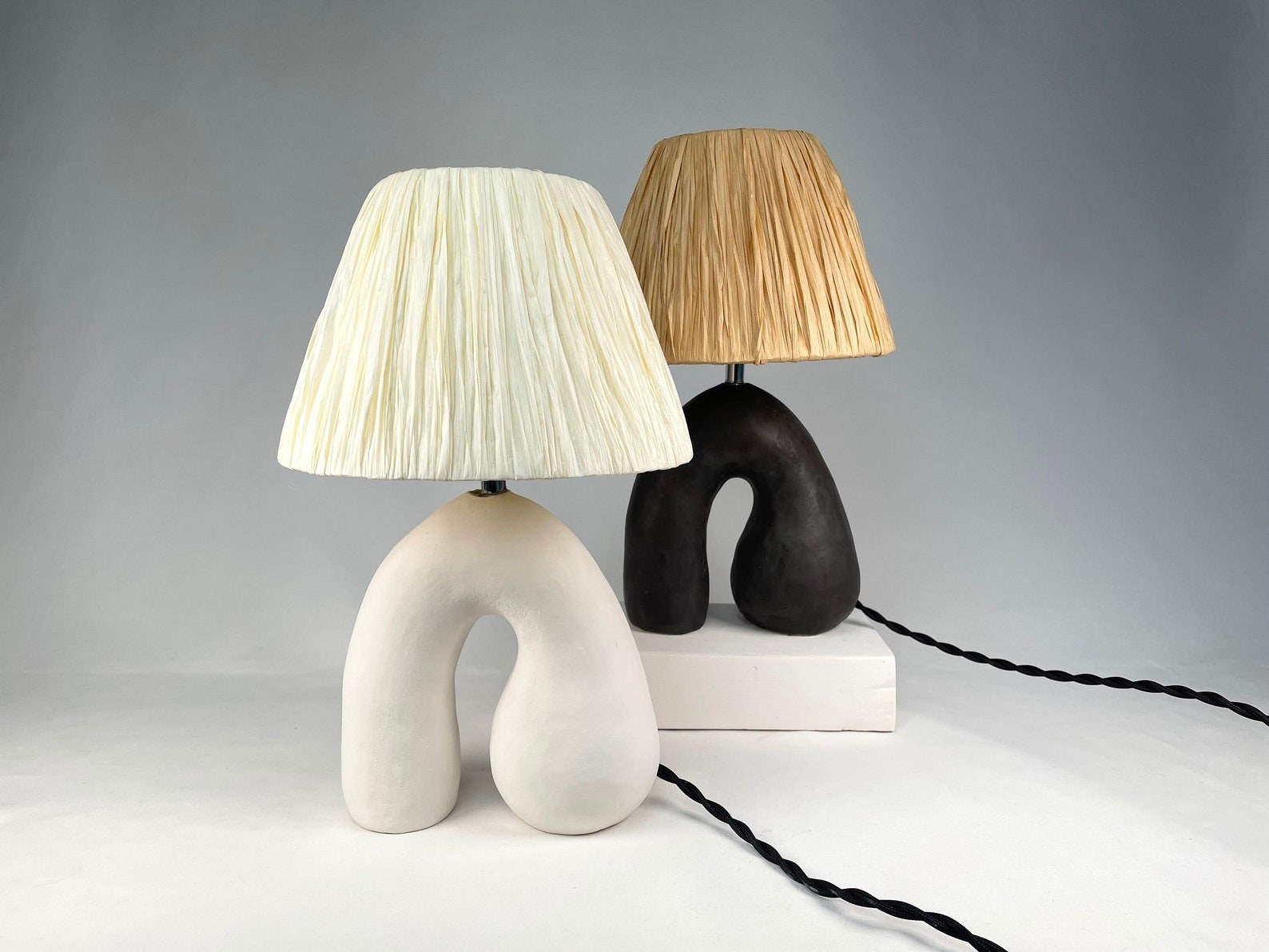 two handmade lamps, one in white base with an ivory shade, and one with a black base with tan shade.