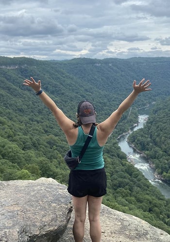 Reviewer wearing the black fanny pack as a crossbody bag while standing on a cliff
