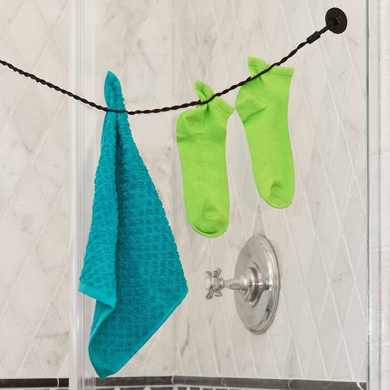 The travel clothesline hanging in a shower and holding a washcloth and a pair of socks