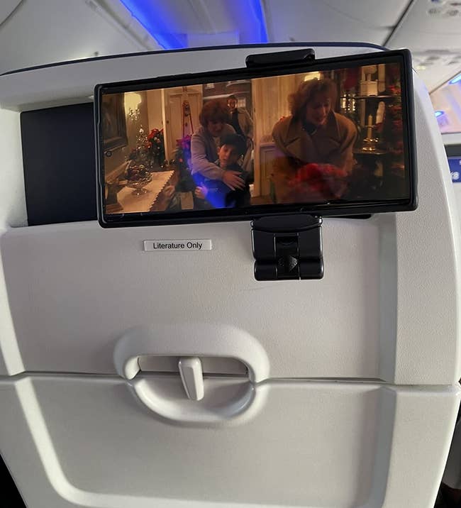 Reviewer photo of the phone mount attached to a stowed seat back tray and holding a phone
