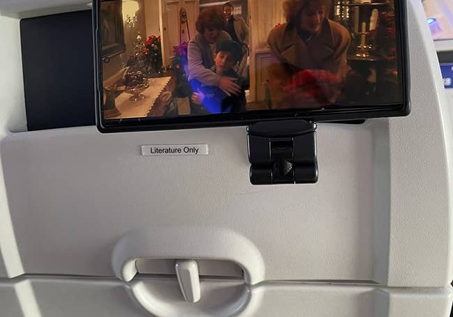 Reviewer photo of the black phone mount attached to a stowed seat back tray and holding a phone