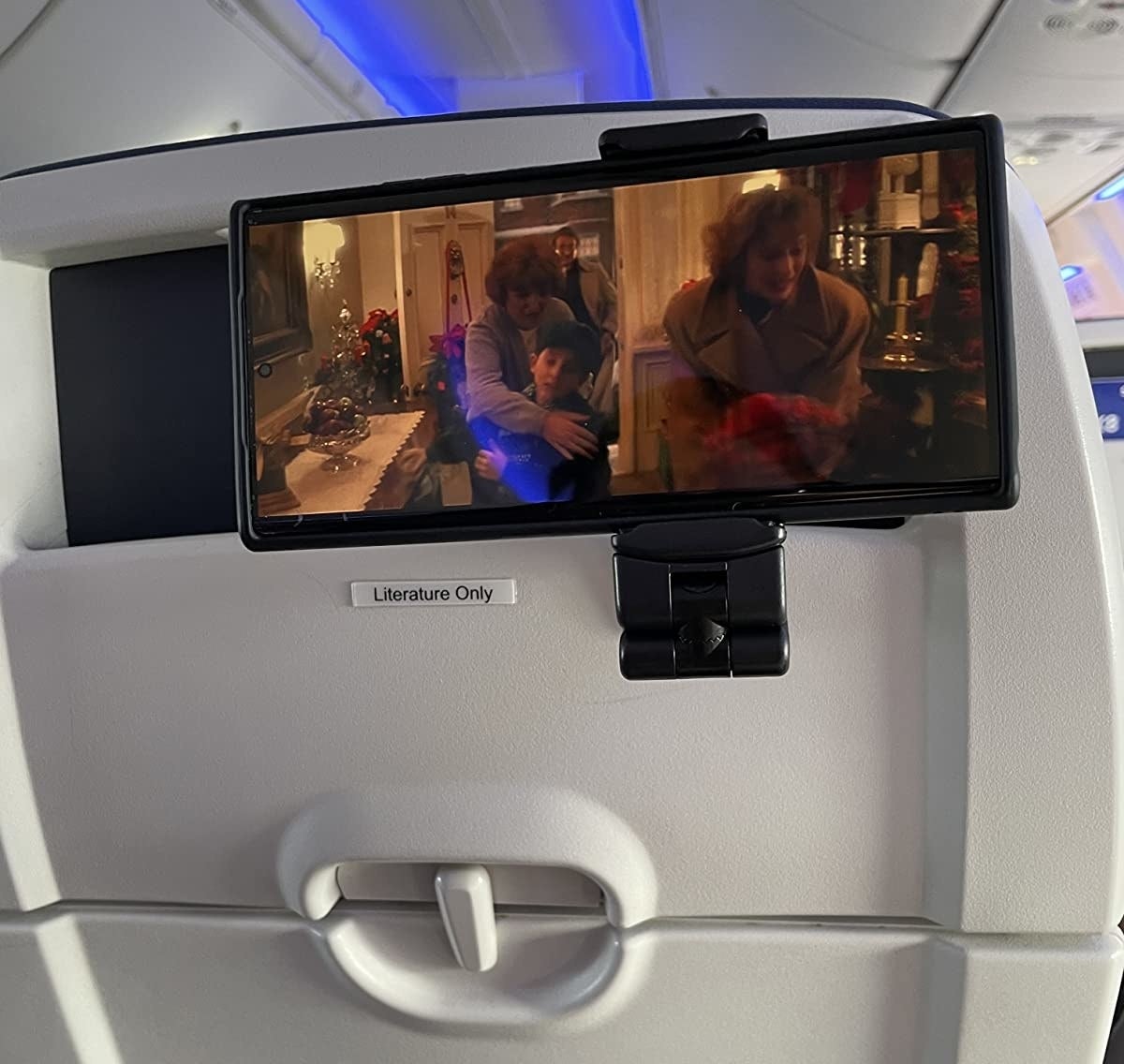 Reviewer photo of the phone mount attached to a stowed seat back tray and holding a phone
