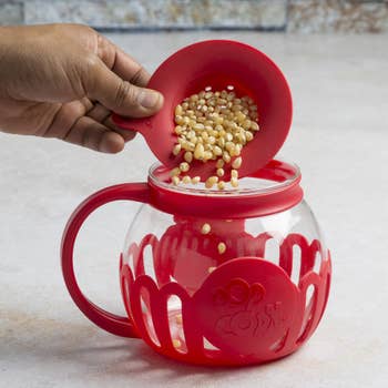 hand pouring popcorn kernels into the glass container