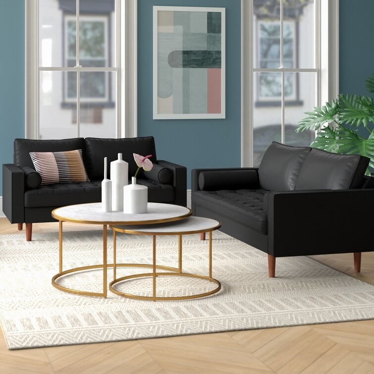 Two black couches around two white and gold circular coffee tables