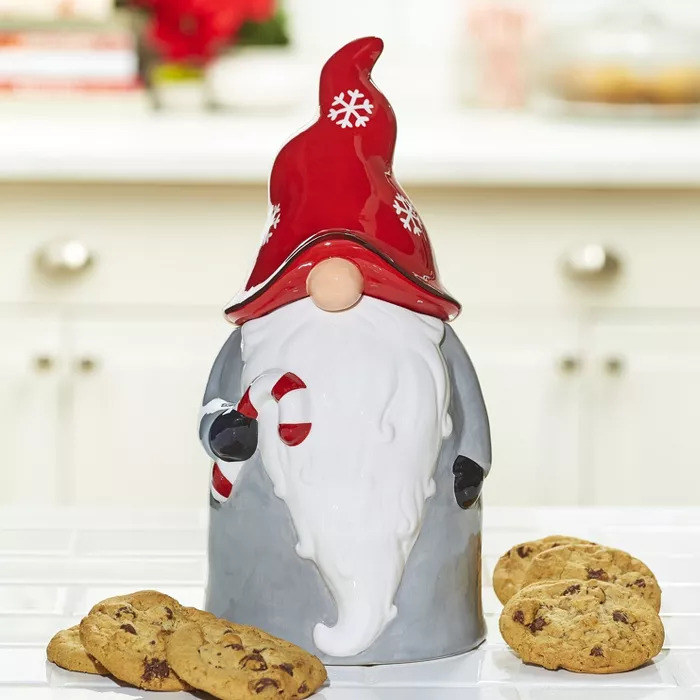 A ceramic Christmas gnome cookie jar sitting on a counter next to some chocolate chip cookies