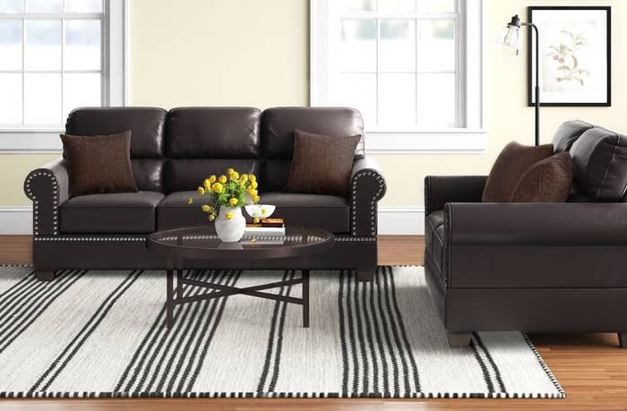Two brown fake leather sofas around a white and brown striped rug and coffee table