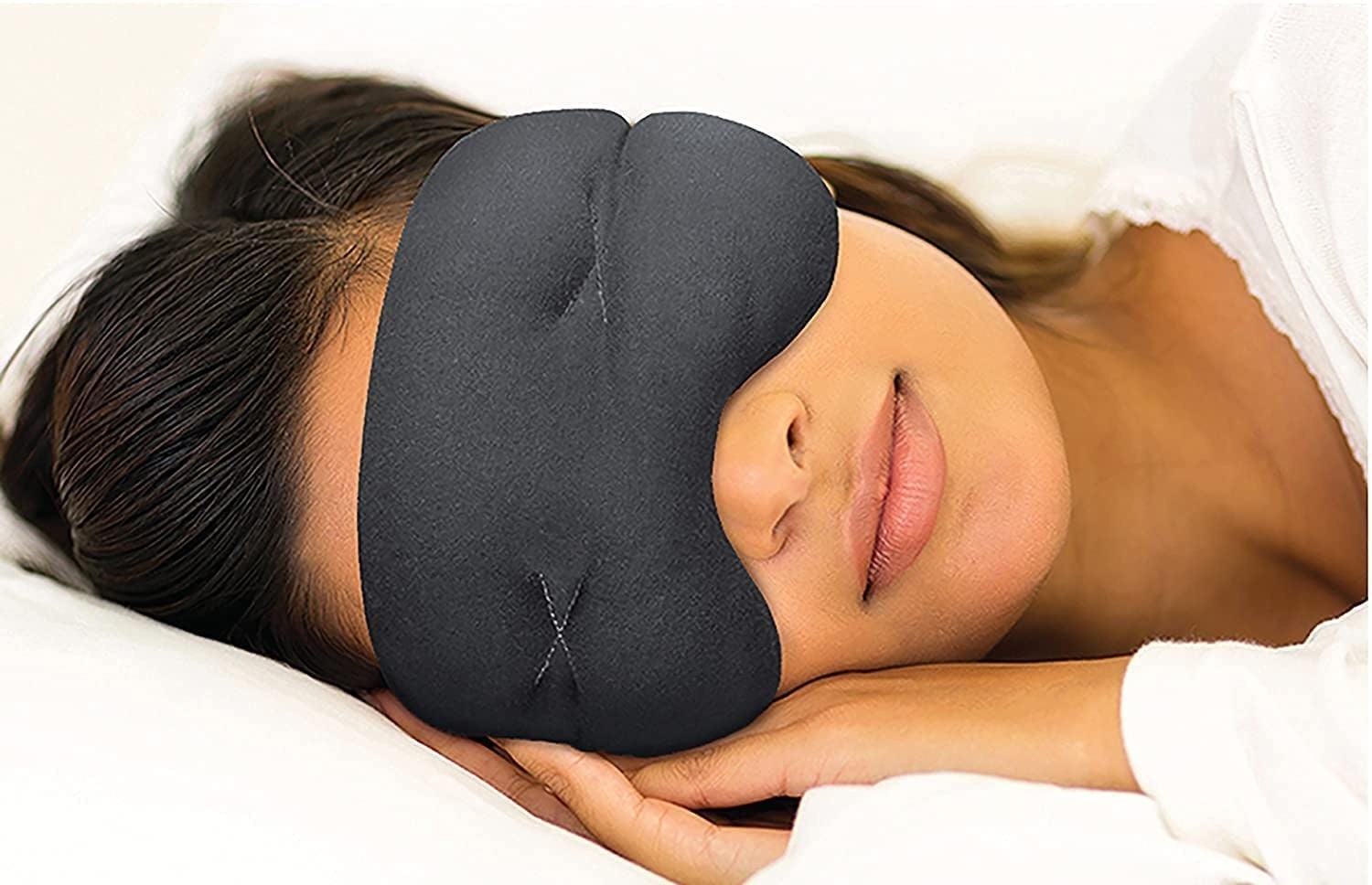 Model wears black mask over their eyes while curled up in bed