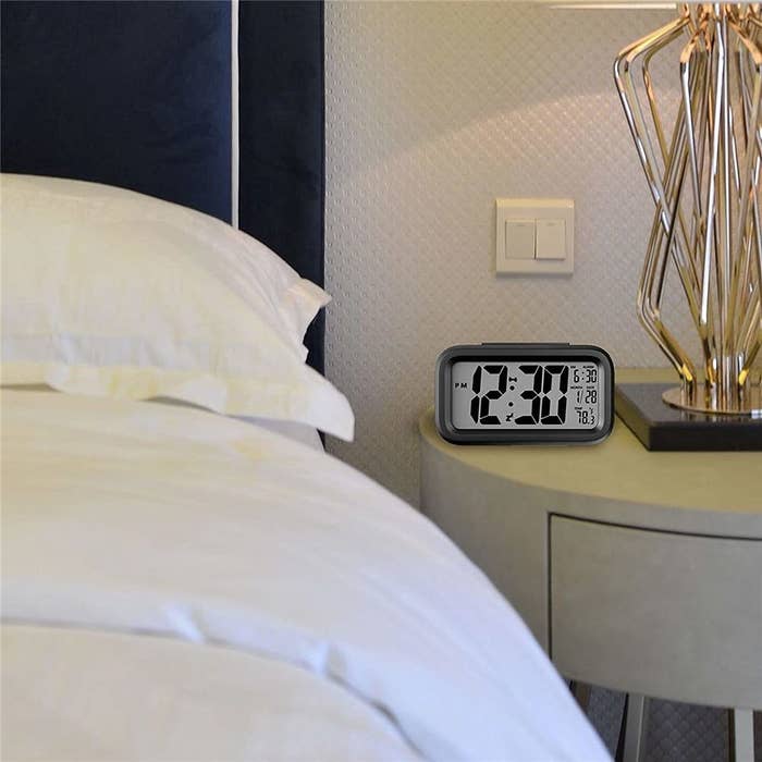 An alarm clock beside a bed on a table