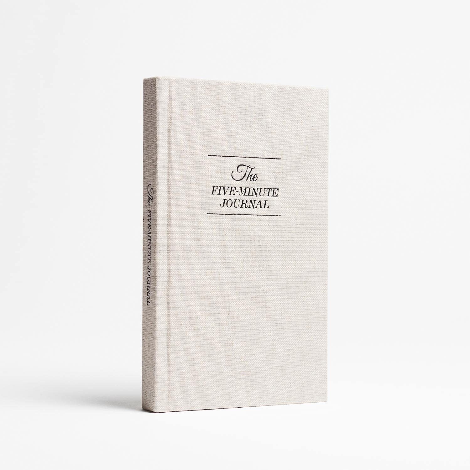 the white journal with black font that reads "The five-minute journal" on the front and on the spine.