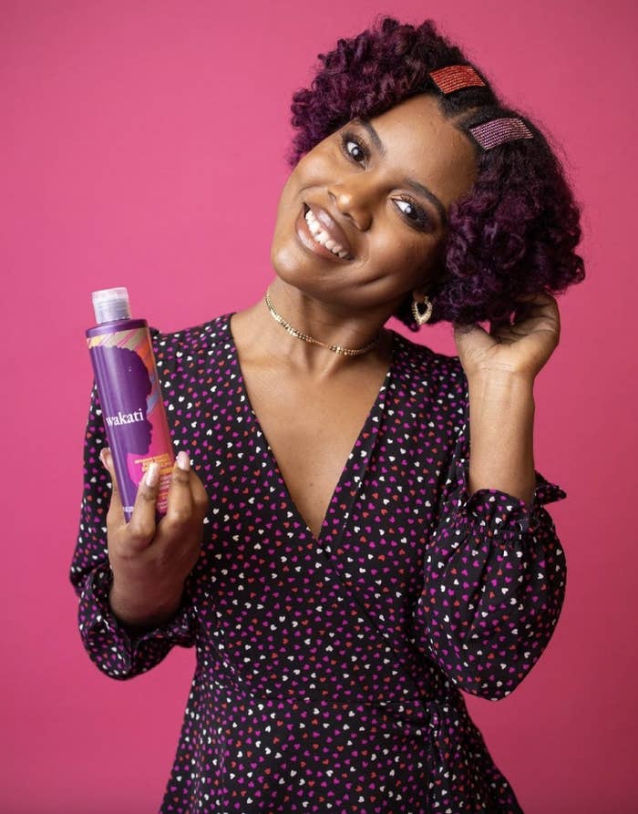 A person with curly hair holding a bottle of hair conditioner