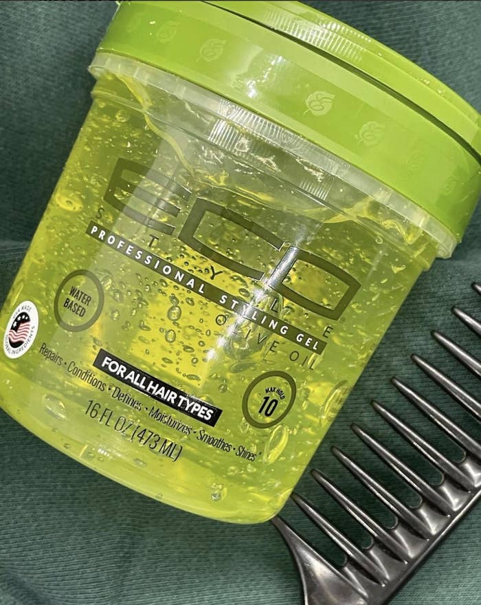 A jar of hair gel with a black wide tooth comb