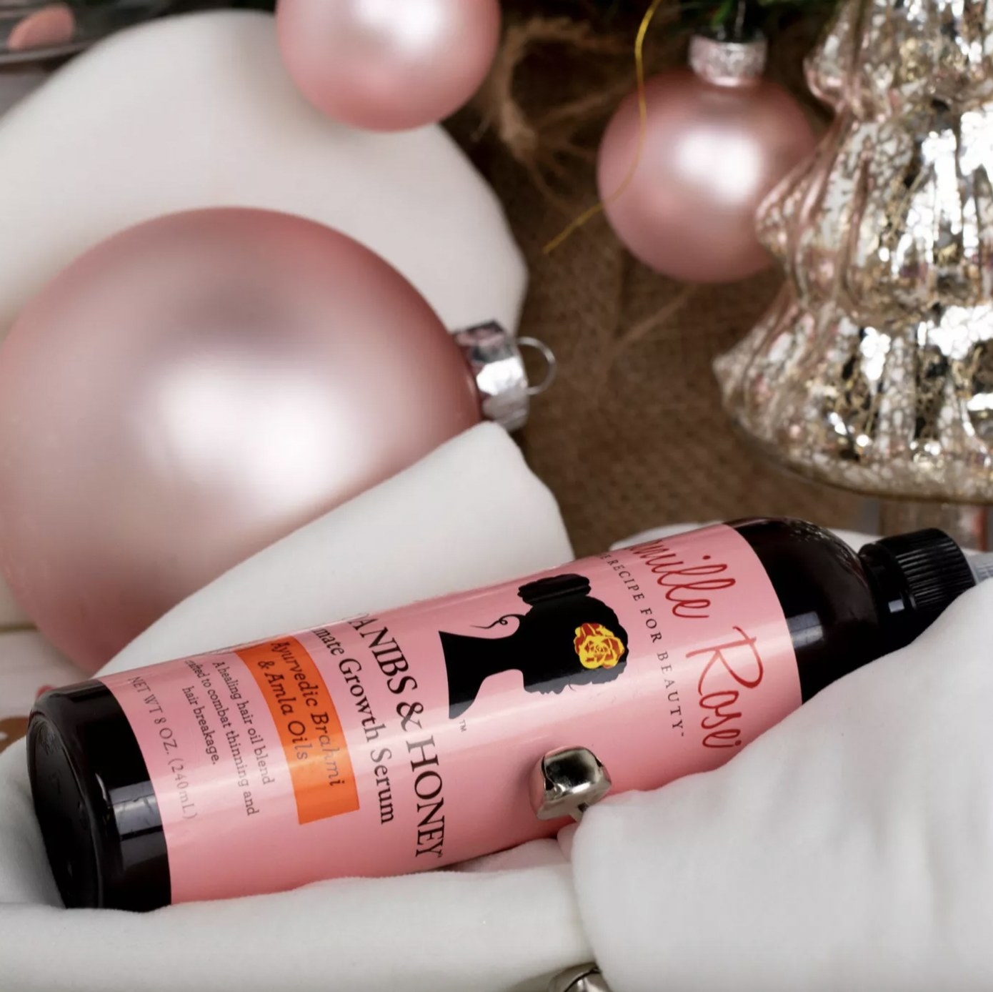A bottle of hair oil and pink and white Christmas ornaments